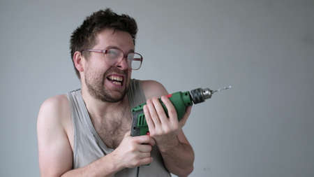 Crazy young man in big glasses pretending that he is drilling neighbours wall at nightの写真素材