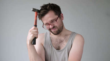 Male builder in big glasses scratches his head with a hammer. I do not know how to repair it.の写真素材