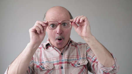Surprised handsome senior man looking through glasses on shock content.