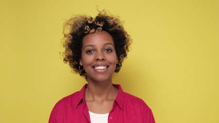 Young african woman with curly hair smiling standing on colored wall. positive facial human emotion.