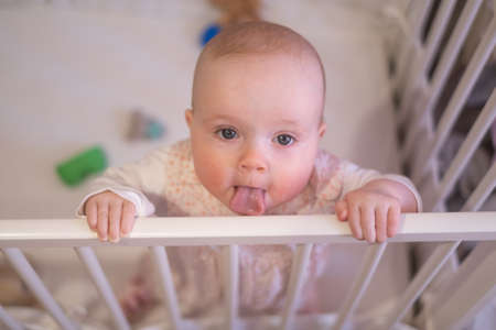 Cute little baby standing in crib at home. Waking up on the morning.の写真素材