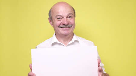 Senior smiling man shows something on empty copyspace on yellow background.の写真素材