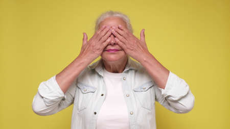 Senior woman closing her eyes waiting for gift on her birthday party. Studio shot on yellow wall.の写真素材