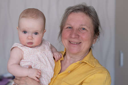 Elderly woman grandmother holding a 7 month baby in her arms at home