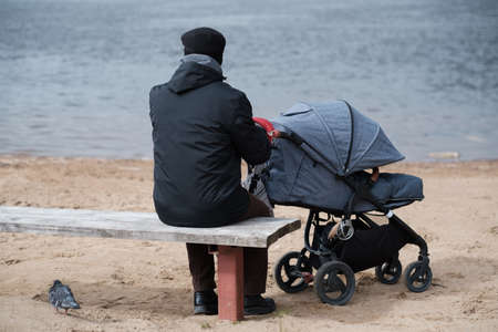 Grandfather walking with a baby stroller on cold and gloomy spring day