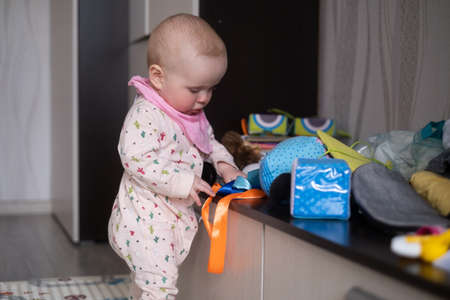 Curious cute toddler girl touching toy, standing alone at the roomの写真素材