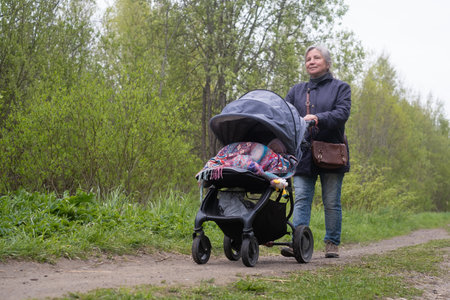 Grandmother walking in spring city park with grandchild with newborn baby in pram.
