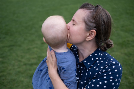 mom holding and kissing baby outdoor on green grass backgroundの写真素材