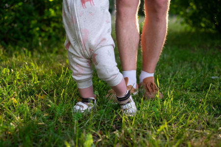 Mom learning baby daughter to walk, first steps in park at summer warm day.の写真素材