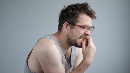 Mature caucasian man looking stressed and nervous with hands on mouth biting nails.