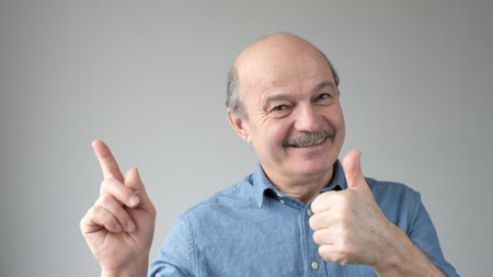 Mature man with happy facial expression pointing aside , presenting copy space.