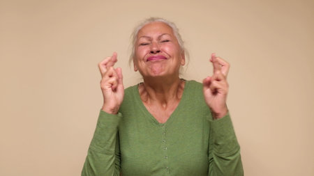 An elderly European woman crosses her fingers for good luck. studio shot