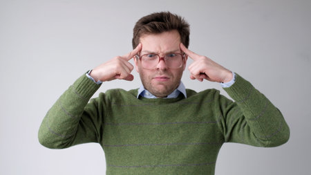 European young man holds his fingers to his temple trying to concentrate and come up with a plan. studio shotの写真素材