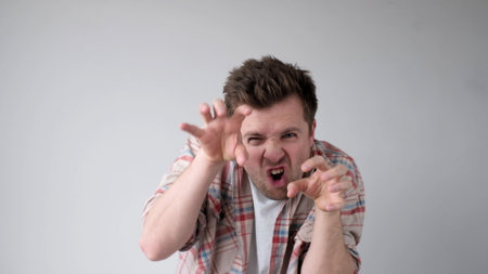 European young man frightens the interlocutor, says boo, and contorts his fingers. studio shotの写真素材