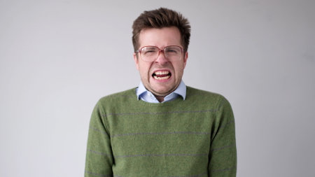 European young man is dissatisfied with the result, he gets angry and contorts a grimace of aggression. studio shotの写真素材