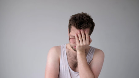 The tired European young man, lacking energy, closes his face with hands. He has no positive emotions. studio shotの写真素材