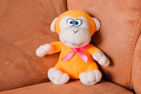 soft yellow toy with red bow sitting on orange sofa