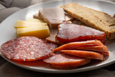 sliced smoked pork, bread, sausage, cheese on plate
