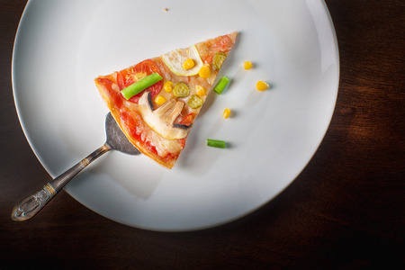 Hot pizza slice with melting cheese on a rustic wooden table.
