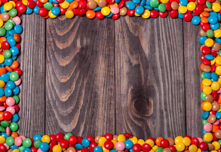 Frame of colorful candy on wood background with space for your text.