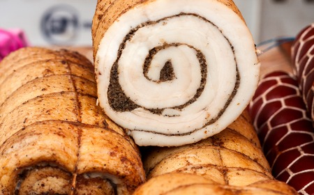 Photo closeup traditional ukrainian preserved salted spicy pepper rolled lard bacon pork fat with garlic and allspice berries on wooden cutting board on timber background.の写真素材