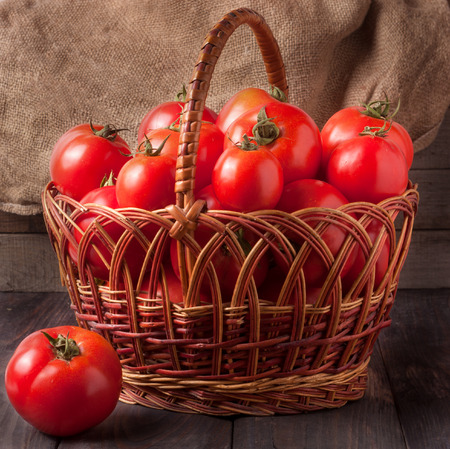 red tomatoes in a wicker basket on a dark wooden table.の写真素材