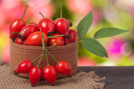 wooden bowl with wild rose on a wooden table with sacking and a blurred background.の写真素材