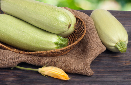 three courgettes with a flower on sackcloth and wooden background.の写真素材