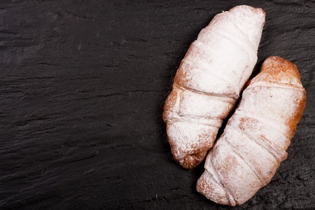 two croissants sprinkled with powdered sugar on black stone background with copy space for your text. Top viewの写真素材