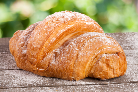 croissant sprinkled with powdered sugar on a wooden board with a blurry garden backgroundの写真素材