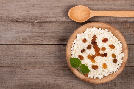 Cottage cheese with raisins in a wooden bowl on old wooden background with copy space for your text. Top view.の写真素材