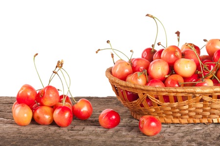 Yellow cherry in a wicker basket on a wooden table with a white background.