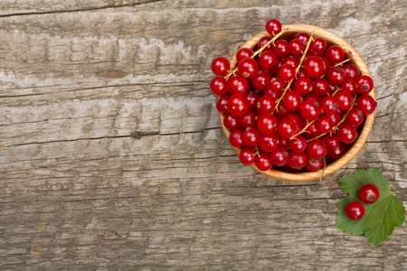 Red currant berries in a wooden bowl with leaf on the old wooden background. Top viewの写真素材