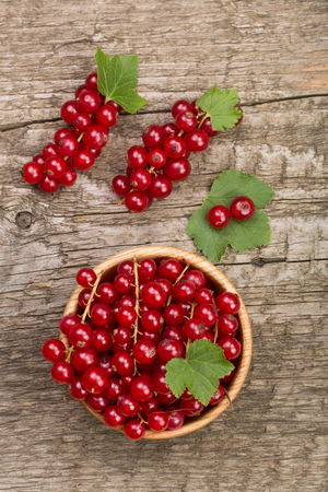 Red currant berries in a wooden bowl with leaf on the old wooden background. Top viewの写真素材