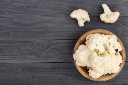 Fresh cauliflower cut into small pieces in wooden bowl on black backgroundの写真素材