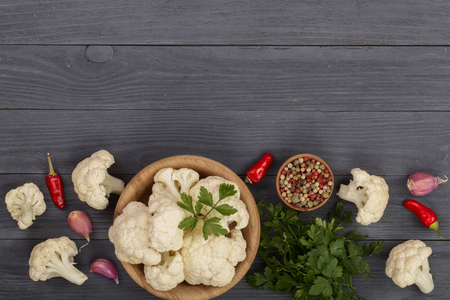 Fresh cauliflower cut into small pieces in wooden bowl with garlic and chili peppers on black wooden background with copy space for your text. Top view.の写真素材