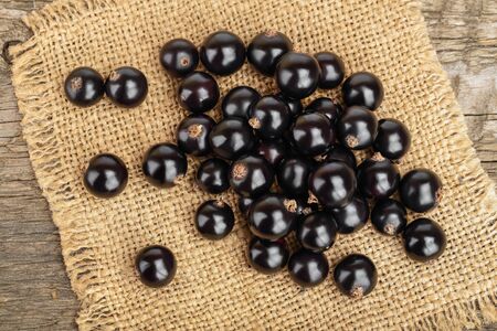 Black currants on burlap and wooden background. Top view. Flat lay pattern.