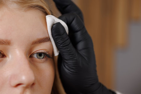 Master eyebrowist makes eyebrow correction to a girl in a beauty salon, close-upの写真素材