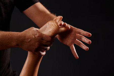 handsome male masseur doing a massage on a girl's leg on a black background, concept of therapeutic relaxing massageの写真素材