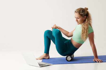 girl holding a massage roller while sitting on the floor and near a laptop, massage roller for fitness and yoga, home online workoutsの写真素材