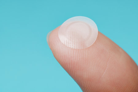 Close-up round acne patch on finger on blue background. Acne patches for treatment of pimple and rosacea close-up. Facial rejuvenation cleansing cosmetologyの写真素材