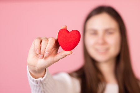 girl holding a heart in her hands close-up on a pink background, the concept of valentine's dayの写真素材