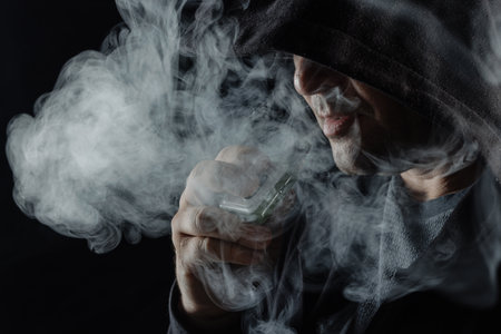 a man smokes a vape electronic cigarette in black clothes on a dark background, close-up, nicotine...