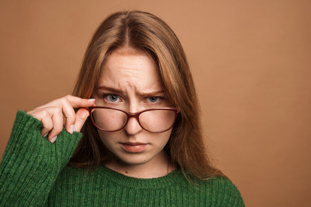 Poor vision concept, portrait of an angry girl in glasses on a beige backgroundの写真素材