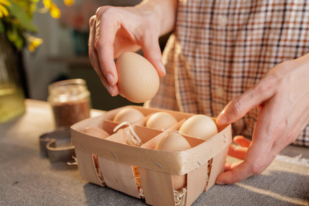 young woman takes chicken egg out of package close-up on kitchen table, home kitchen background,...
