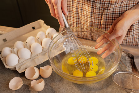 Close-up of female hands beating eggs with a hand whiskey in a transparent bowl against the...