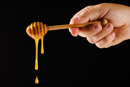 hand close up holding spoon with honey flowing and dripping on dark background, beekeeping concept, natural medicineの写真素材