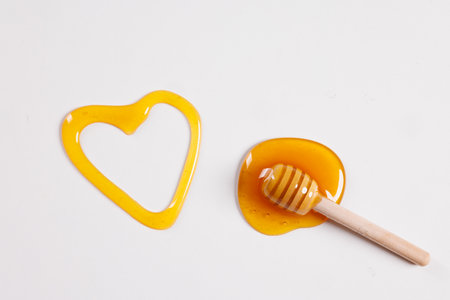 honey spoon with spilled honey in the shape of a heart on a white background top view, concept of love for the health of the bodyの写真素材
