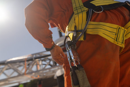 A close-up of a worker wearing a safety harness with a yellow strap, preparing to climb or work at...