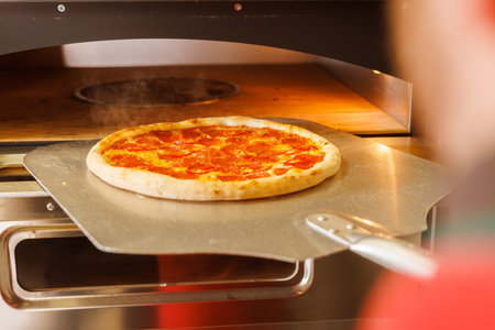 A freshly baked pizza being taken out of a pizza oven using a pizza peel.の写真素材